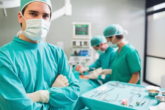 Surgeon with arms crossed looking at camera with colleagues performing in background.jpeg